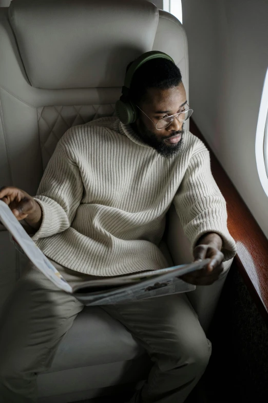 a man sitting in an airplane reading a magazine, pexels contest winner, afrofuturism, he is wearing a brown sweater, jaylen brown, nipsey hussle, feels good man