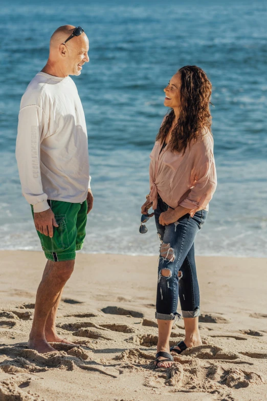 a man and woman standing on a beach next to the ocean, wearing cargo pants, scene from a movie, curls, hollister ranch