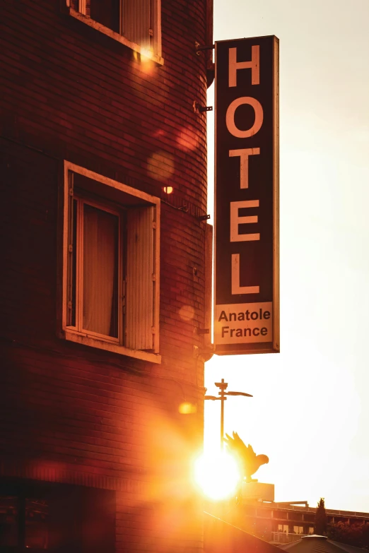 a hotel sign hanging from the side of a building, a photo, by Andrée Ruellan, unsplash, sunset backlight, anomalisa, french, historical photo