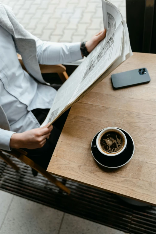 a man sitting at a table reading a newspaper next to a cup of coffee, trending on unsplash, private press, inspect in inventory image, gentleman, sitting on top a table, high angle close up shot