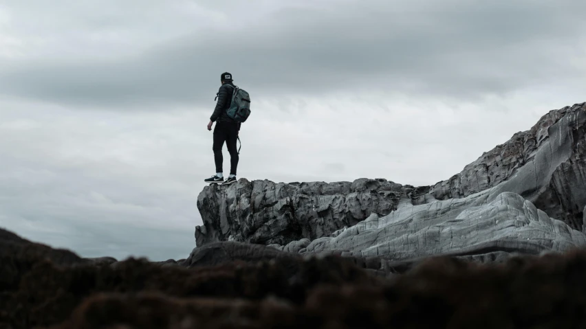 a man standing on top of a large rock, pexels contest winner, overcast gray skies, with a backpack, grey and dark theme, grey