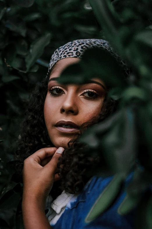 a woman standing in front of a bush with her hand on her chin, an album cover, trending on pexels, renaissance, mixed-race woman, wearing a head scarf, large dark eyes, curls and curves