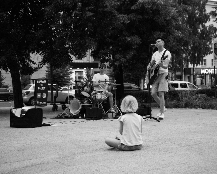 a little girl sitting on the ground next to a man, an album cover, by Greg Spalenka, band playing, tri - x pan, live performance, summer street