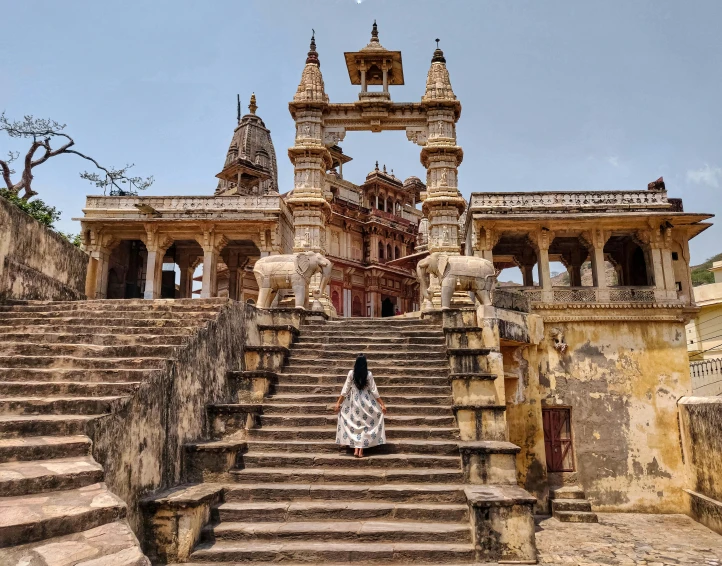 a woman standing in front of a large building, sitting on temple stairs, a majestic gothic indian dragon, dry archways and spires, 2019 trending photo