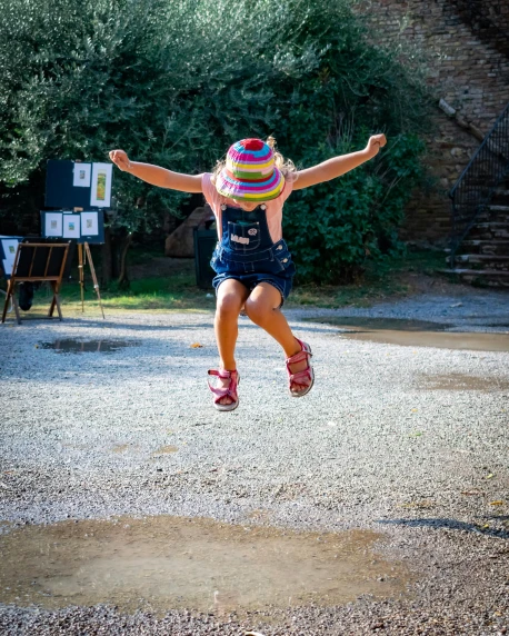 a little girl that is jumping in the air, by Arabella Rankin, pexels contest winner, lourmarin, 5k, well built, wearing a silly hat