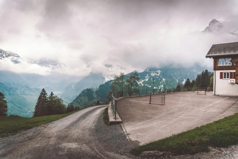 a small building sitting on the side of a road, by Sebastian Spreng, pexels contest winner, 4 k cinematic panoramic view, downhill landscape, overcast, driveway