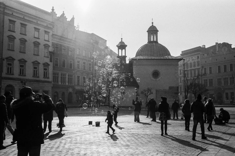 a black and white photo of a crowd of people, by Gusztáv Kelety, pexels contest winner, in a square, bubble, sunny winter day, old city