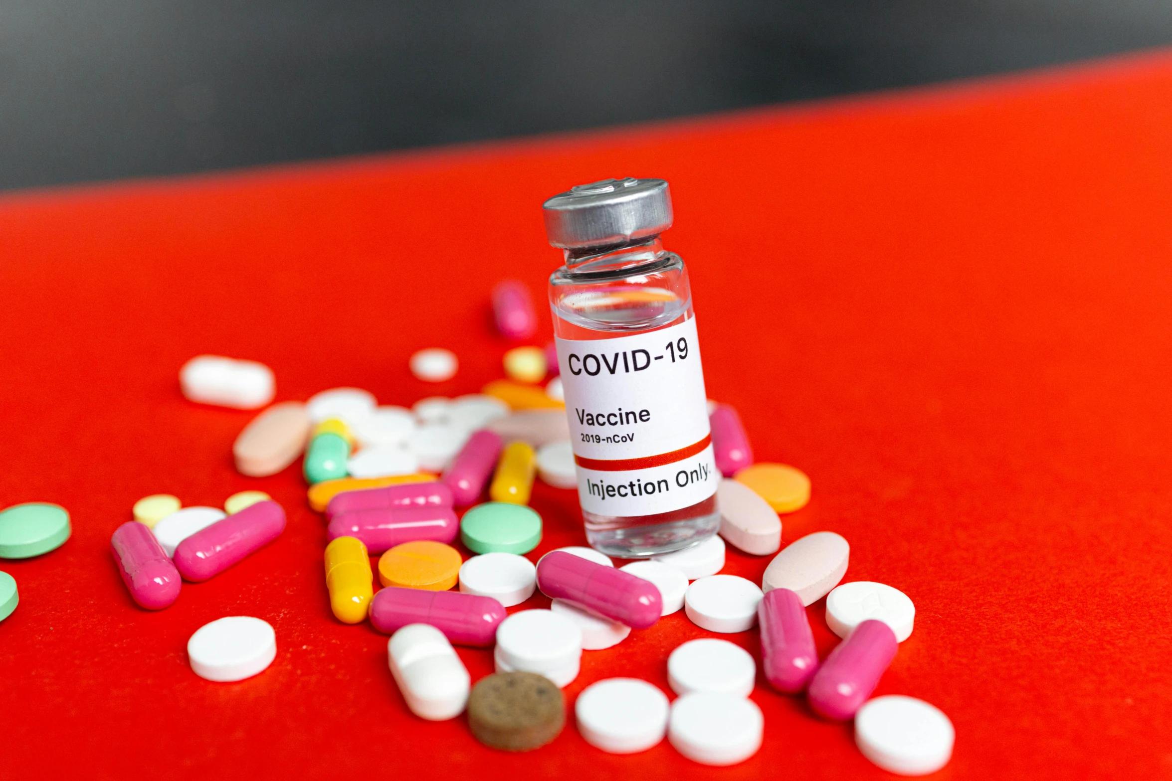 a bottle filled with pills sitting on top of a red table, coronavirus, multi - coloured, profile image, syringe