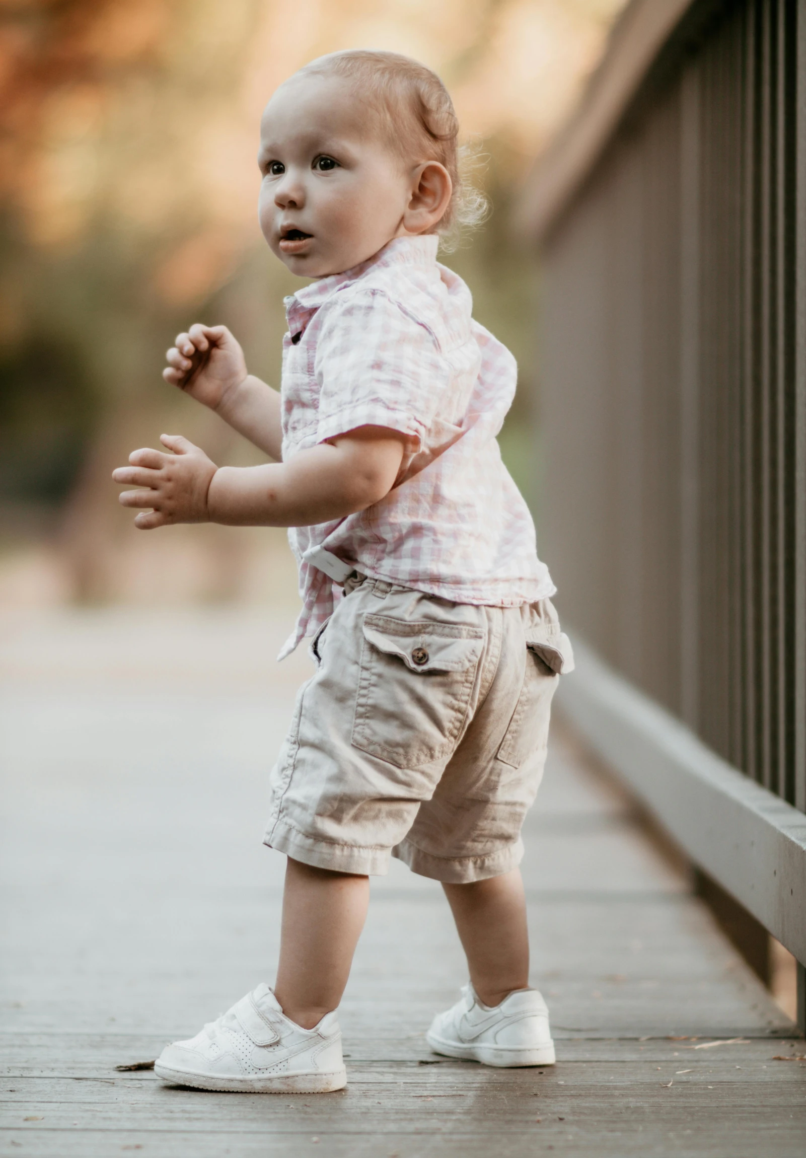 a small child standing on a wooden bridge, by Tom Bonson, happening, tan shorts, on the sidewalk, soft lighting and focus, wearing a linen shirt