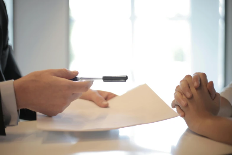 a person sitting at a table with a pen and paper, reaching out to each other, selling insurance, official screenshot, no blur
