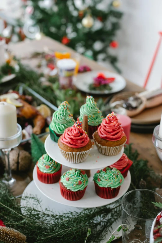 a table topped with cupcakes covered in frosting, vibrant red and green colours, food styling, holiday vibe, mid - shot