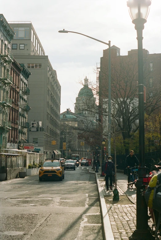 a man riding a bike down a street next to tall buildings, metropolitan museum of art, busy small town street, image from afar, orthodox