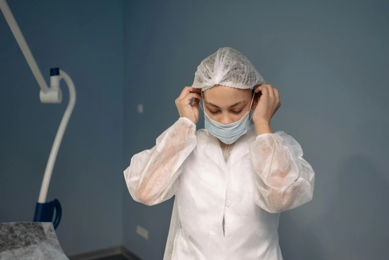 a woman in a medical gown adjusts her hair, pexels contest winner, clean room, avatar image, working clothes, wearing hoods