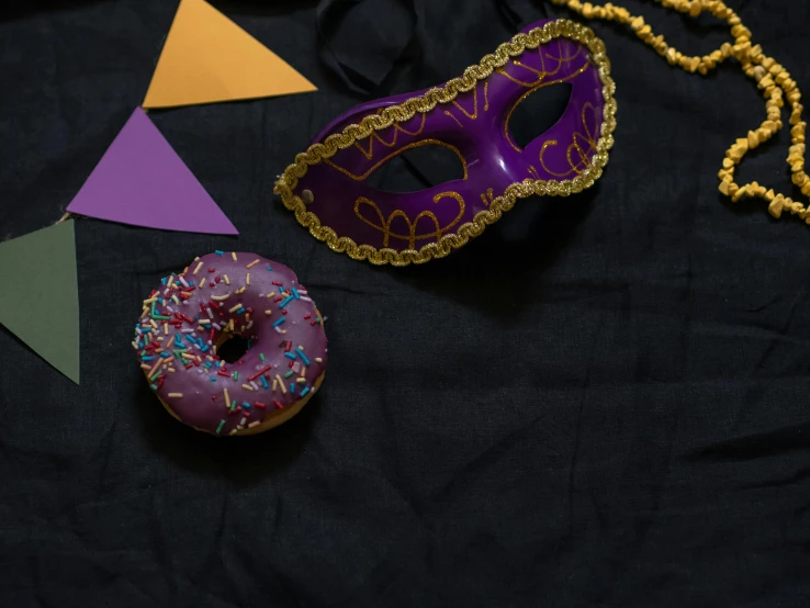 a purple mask sitting on top of a table next to a donut, trending on pexels, decorative dark blue clothing, background image, jeweled costume, a high angle shot