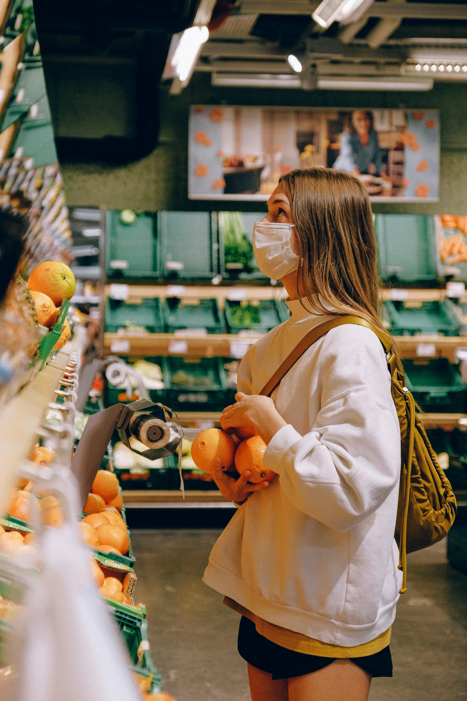 a woman wearing a face mask in a grocery store, pexels contest winner, happening, holding a tangerine, people walking around, 🌸 🌼 💮, a green