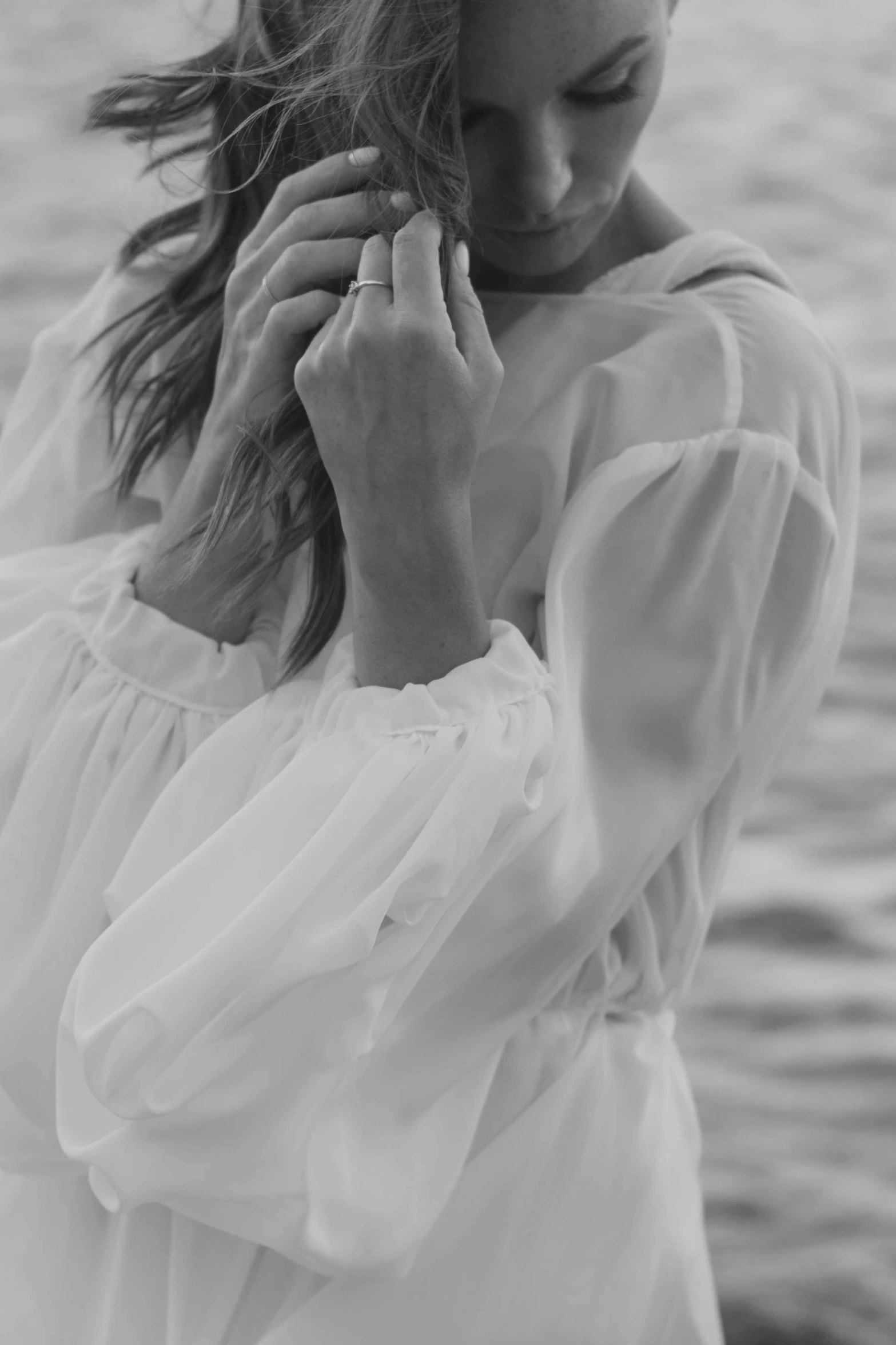 a woman standing in front of a body of water, a black and white photo, romanticism, white dress shirt, zoomed in shots, sheer fabrics, 15081959 21121991 01012000 4k