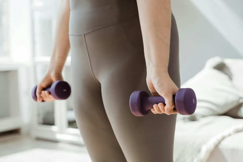 a close up of a person holding a pair of dumbbells, by Emma Andijewska, trending on pexels, purple bridges with leggins, holding a staff, sydney hanson, smooth contours