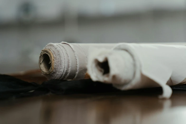 a roll of fabric sitting on top of a wooden table, inspired by ashley wood, unsplash, renaissance, healing tubes, smokey burnt envelopes, clay material, cream paper