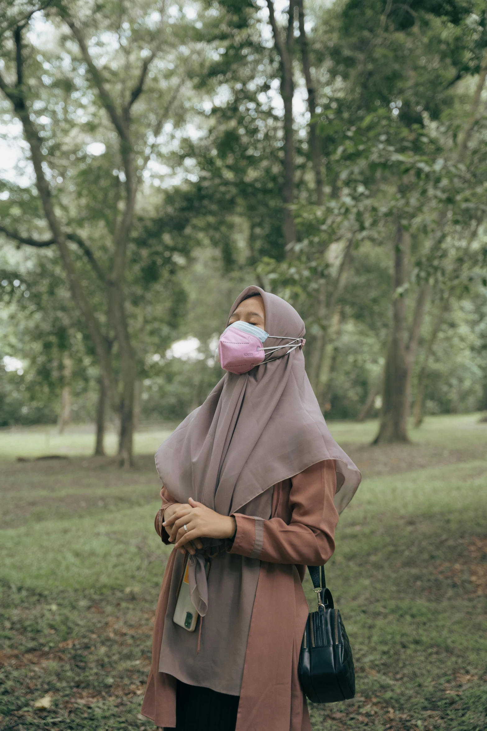 a woman wearing a face mask standing in a park, by Basuki Abdullah, unsplash contest winner, hyperrealism, ((pink)), film color photography, grey, humid