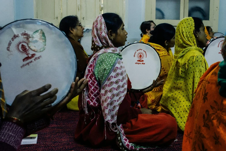 a group of women sitting on the floor playing musical instruments, pexels contest winner, hurufiyya, holding khopesh and shield, photo still of behind view, india, round-cropped