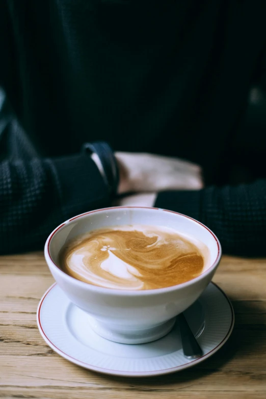 a person sitting at a table with a cup of coffee, by Austin English, cappuccino, crossed arms, uncropped, wide neck