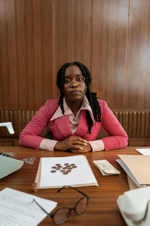 a woman sitting at a table with papers on it, an album cover, dark skinned, in a courtroom, with piles of coins around it, high quality photo