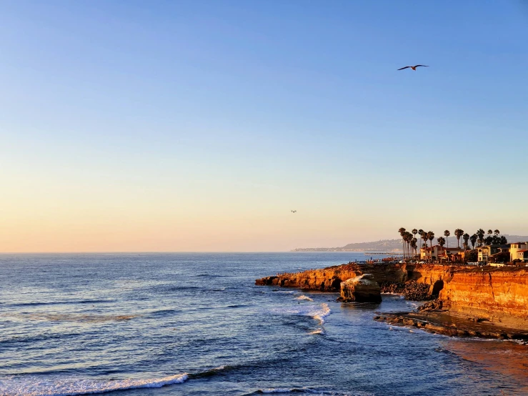 a bird flying over a beach next to the ocean, the city of santa barbara, ocean and rock landscape, guide, a cozy