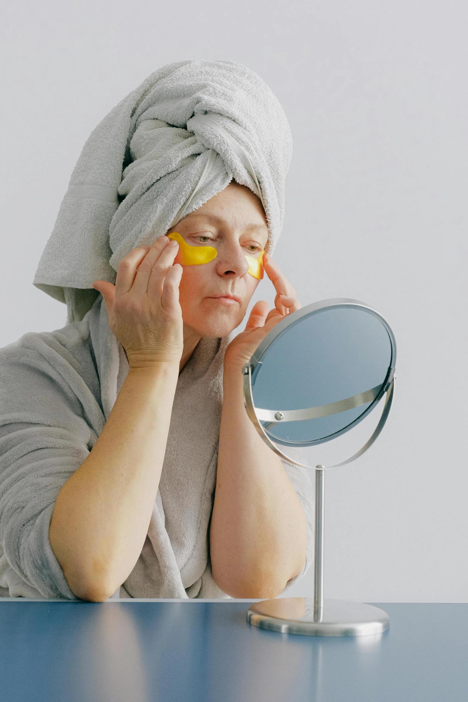 a woman sitting at a table with a towel on her head, a picture, pexels, with a mirror, silver and yellow color scheme, with a white background, healthcare