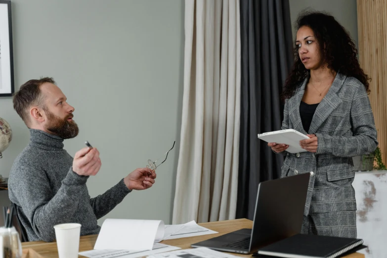 a man and a woman sitting at a table in front of a laptop, standing on a desk, convincing, profile image, grey