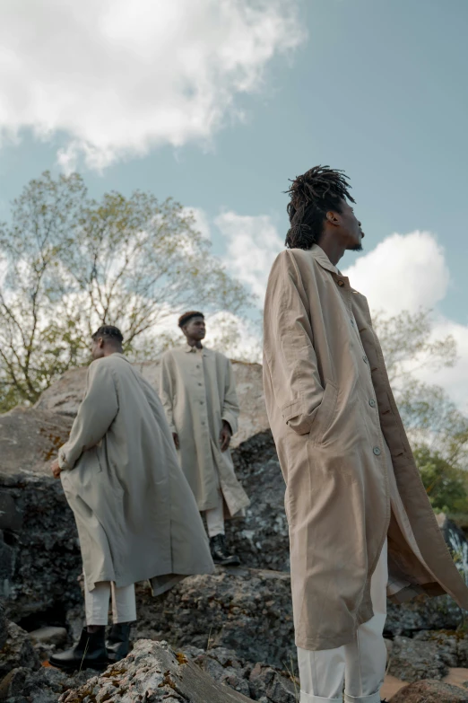 a group of men standing on top of a pile of rubble, an album cover, by Caro Niederer, unsplash, afrofuturism, wearing a long beige trench coat, jamaica, ( ( theatrical ) ), standing on a hill