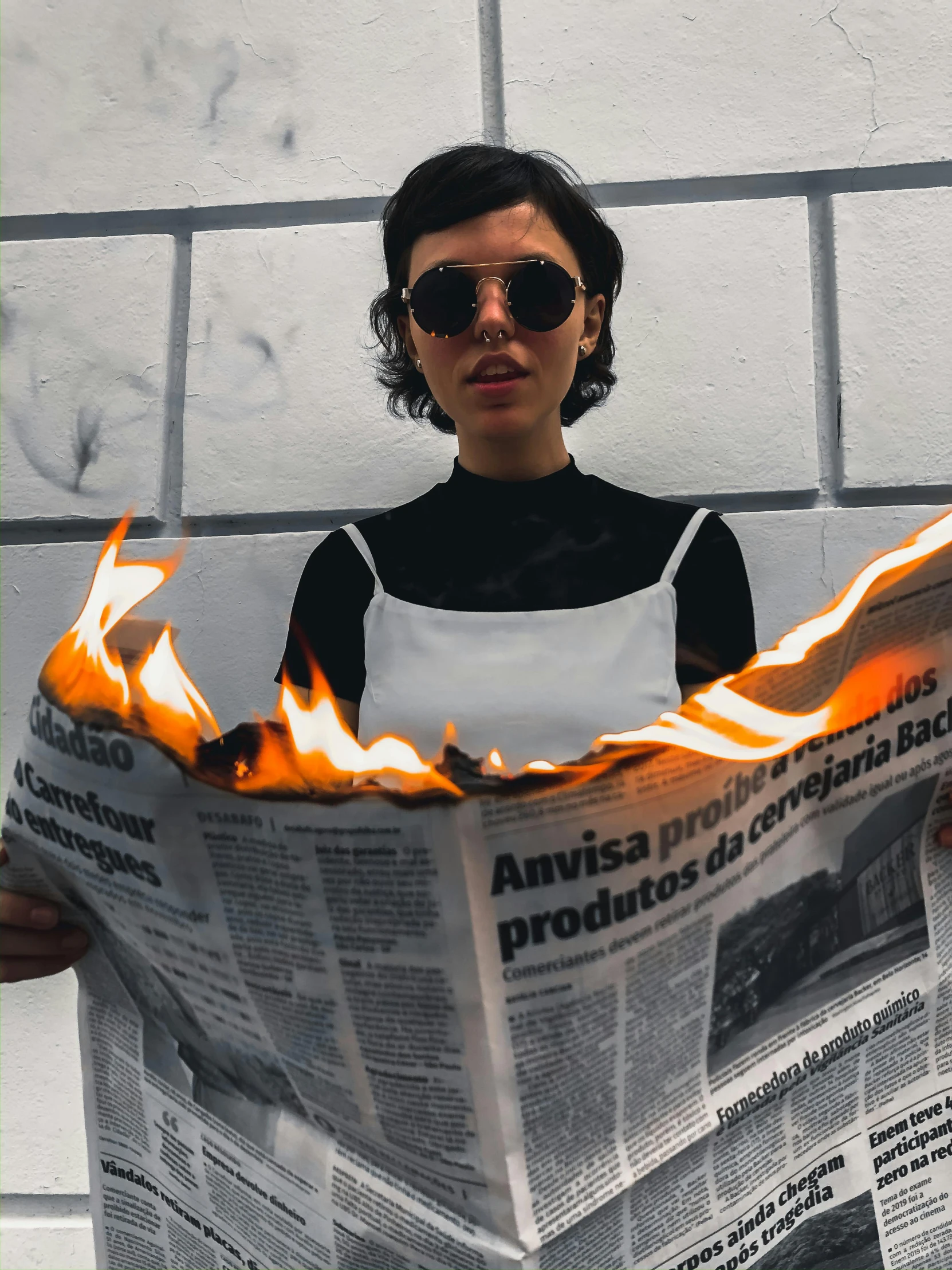 a woman holding a burning newspaper in front of a brick wall, inspired by Elsa Bleda, trending on unsplash, surrealism, woman made of black flames, charli xcx, in sao paulo, cooking it up