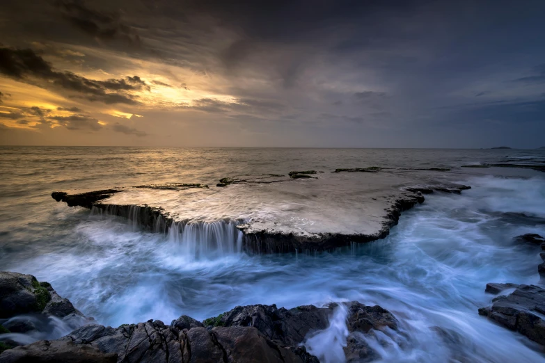 a large body of water sitting on top of a rocky beach, by Ibrahim Kodra, unsplash contest winner, water cascading, liquid metal, seaview, just after rain