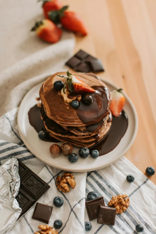 a stack of pancakes sitting on top of a white plate, by Julia Pishtar, pexels contest winner, fully chocolate, natural wood top, fruit, full product shot