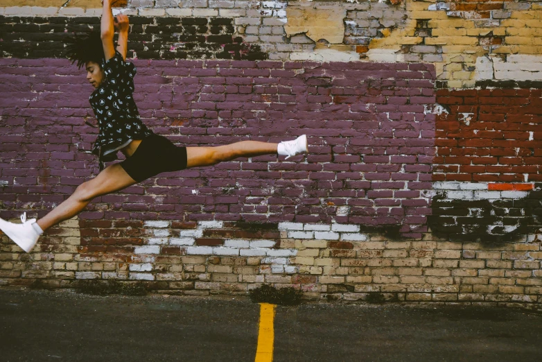 a woman jumping in the air in front of a brick wall, pexels contest winner, arabesque, background image, sarcastic pose, pointe poses, highly upvoted