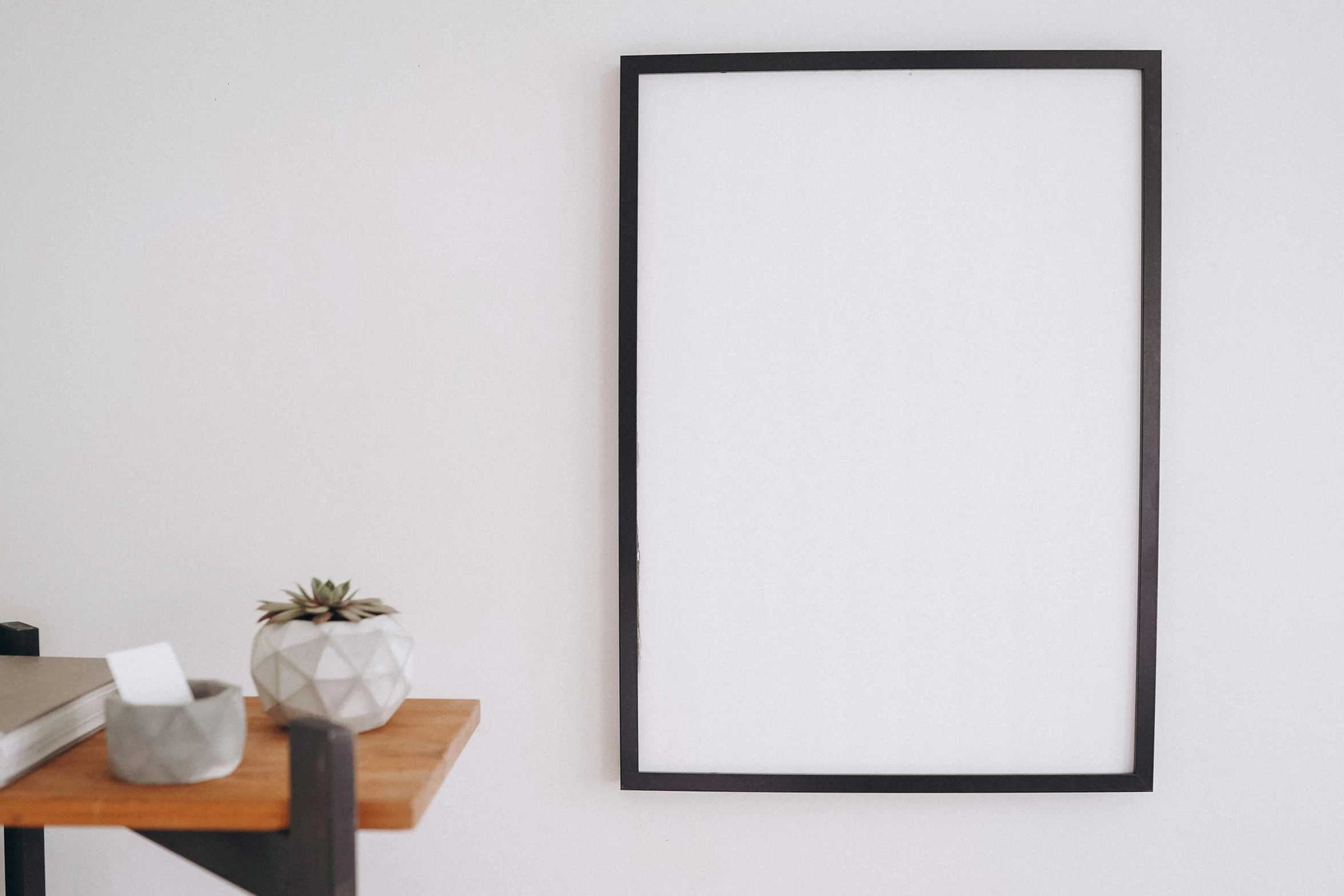 a picture frame sitting on top of a wooden table, a minimalist painting, trending on unsplash, postminimalism, whiteboard, white wall, black furniture, metal framed portal