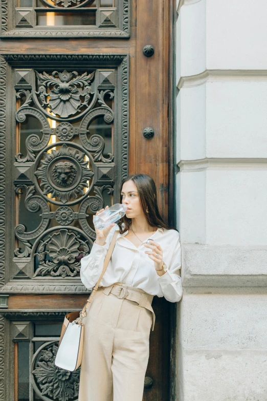 a woman standing in front of a wooden door, woman drinking coffee, cream colored blouse, in moscow centre, hydration