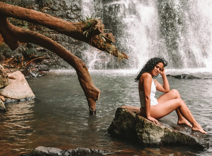 a woman sitting on a rock in front of a waterfall, with brown skin, is wearing a swimsuit, sydney park, samoan features