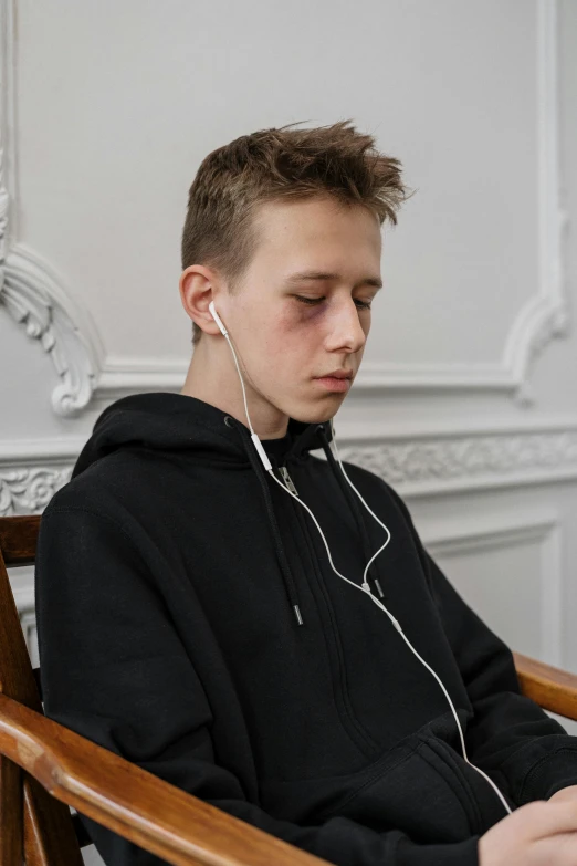 a young man sitting in a chair with headphones on, trending on pexels, hyperrealism, portrait a 1 5 - year - old boy, earbuds jewelry, hammershøi, disappointed