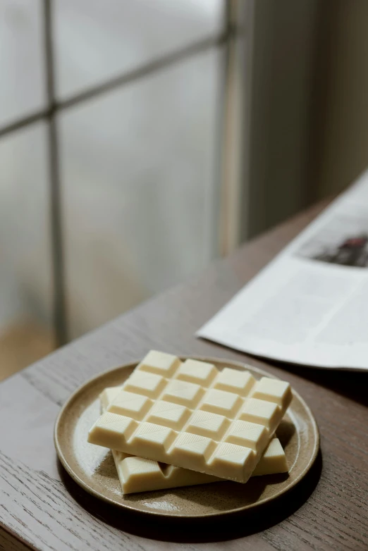 a plate of chocolate sitting on top of a wooden table, mingei, white, squares, candid photograph, tan