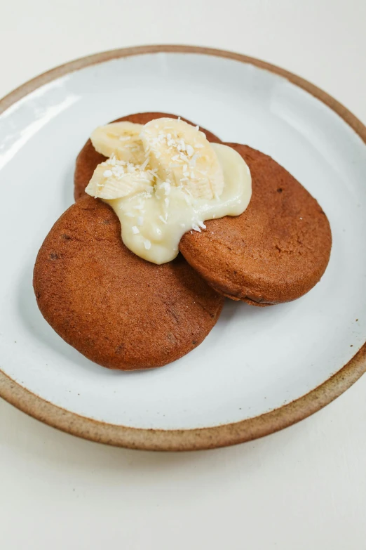 a couple of cookies that are on a plate, clumps of bananas, sleek white, butter, reddish