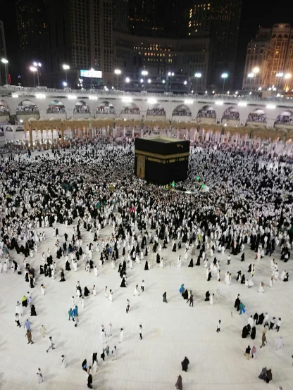 a large crowd of people standing around a building, mecca, during the night, at night time