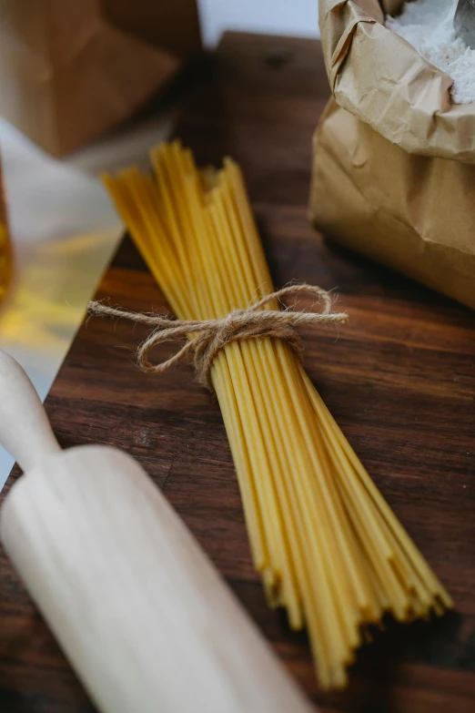 a wooden cutting board topped with pasta and a rolling pin, a portrait, pexels, ribbon, spaghetti, up close shot, petite