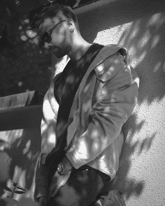 a black and white photo of a man leaning against a wall, a black and white photo, hurufiyya, in a black hoodie, wearing shades, wearing a fancy jacket, profile image