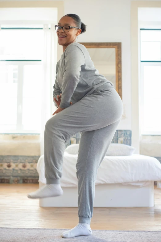 a woman standing on a yoga mat in a room, happening, wearing a baggy pajamas, light grey, dynamic movement, curvacious