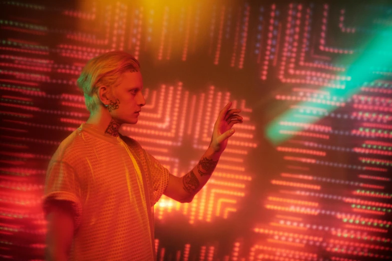 a woman standing in front of a computer screen, inspired by Mike Winkelmann, pexels, holography, jamie campbell bower, still from a music video, blonde man, light emitting from fingertips