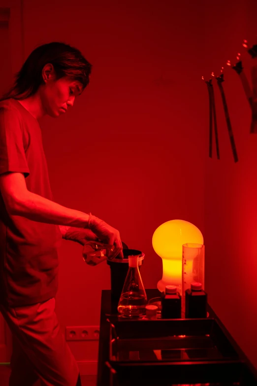 a man standing in front of a red light, by Doug Ohlson, kinetic art, working in her science lab, alchemical still made from clay, photo taken in 2018, mixing drinks