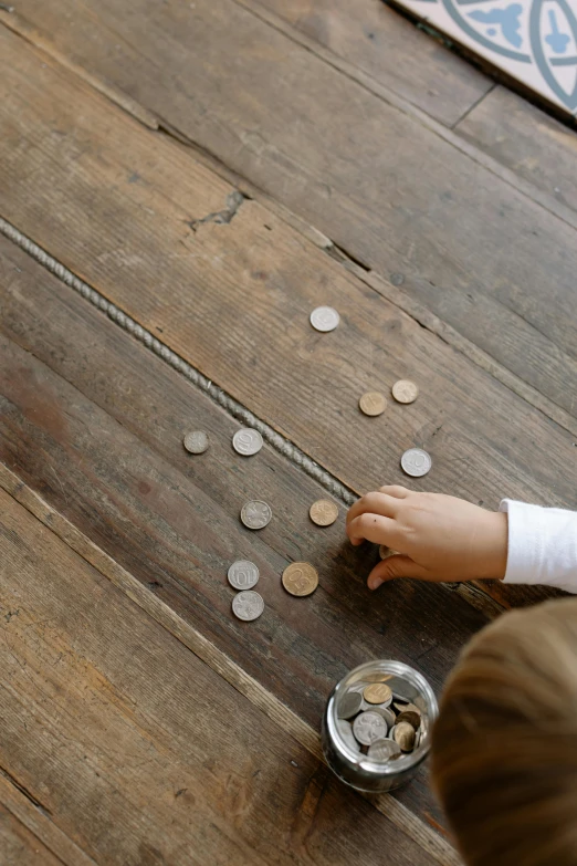 a child playing with coins on a wooden floor, curated collections, silver, petite, brown