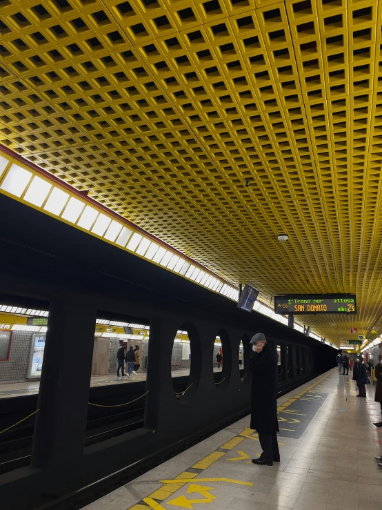 a group of people standing on a train platform, yellow and black color scheme, complex ceiling, from the distance, tiled