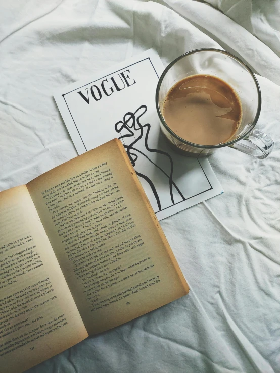 an open book sitting on top of a bed next to a cup of coffee, by Lucia Peka, pexels contest winner, art nouveau, vogue cover poses, vintage 9 0 s print, featured on vogue, soft vinyl