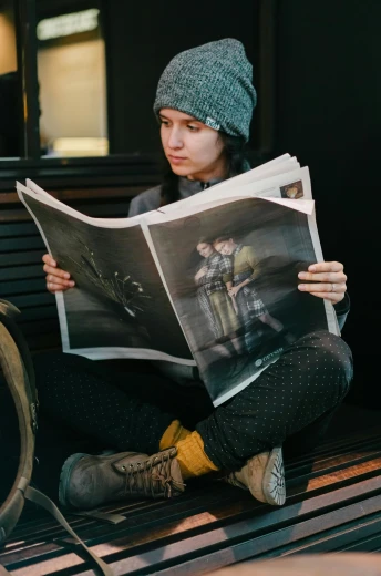 a woman sitting on a bench reading a newspaper, a picture, by Adam Marczyński, unsplash contest winner, portrait of max caulfield, indoor picture, wearing a grey wizard hat, full - length photo
